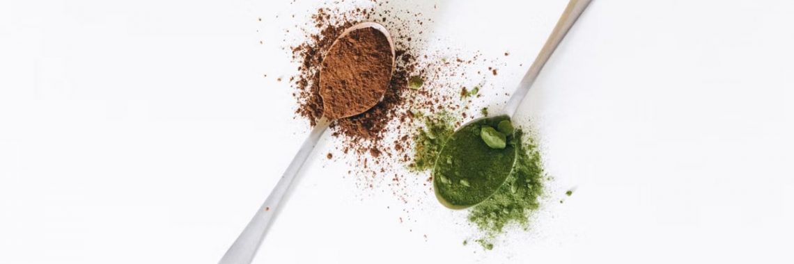 Close-up of spoons with cocoa and matcha powder on a white surface, perfect for food and health themes.